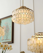 Seen from below, a Clérachic chandelier glows warm, its tiers of shell teardrops framed with an angel figure and a painting at the edge.
