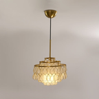 A Clérachic chandelier on a ceiling plate and black cord, with a short gold rod and three rings of shell teardrops lit warm.