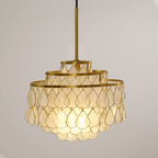Close to the camera, this Clérachic chandelier on a black cord shows large capiz shell teardrops glowing warm in gold wire.