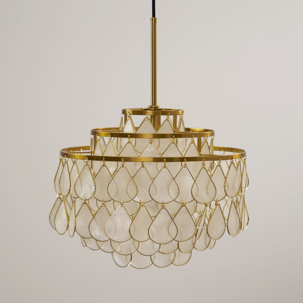 This Clérachic chandelier hangs unlit on a gold rod, its large teardrop shell discs held in fine gold wire on a pale backdrop.