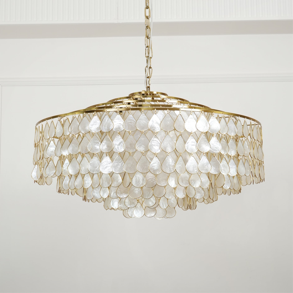 A wide, pale Clérachic chandelier on a chain, with five tiers of pearly teardrop shell discs on gold rings, on a white wall.