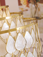 Close view of the gold wire frame and teardrop shell discs on this Clérachic chandelier, with the tiers blurred behind.