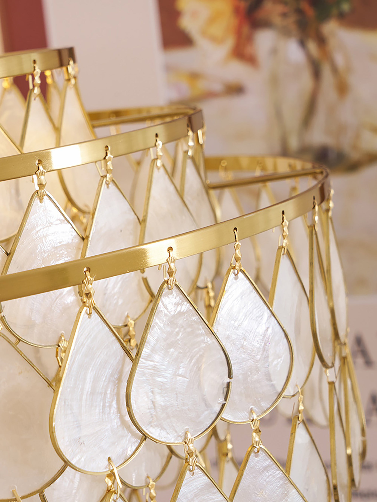 Close view of the gold wire frame and teardrop shell discs on this Clérachic chandelier, with the tiers blurred behind.