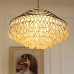 This Clérachic chandelier lit and seen from below, its gold-framed teardrop shell discs glowing warm in front of an arched painting.