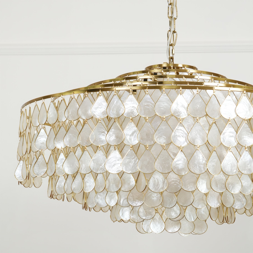The pearly side of this Clérachic chandelier, with rows of white shell teardrops on gold rings, hung from a chain against a white wall.