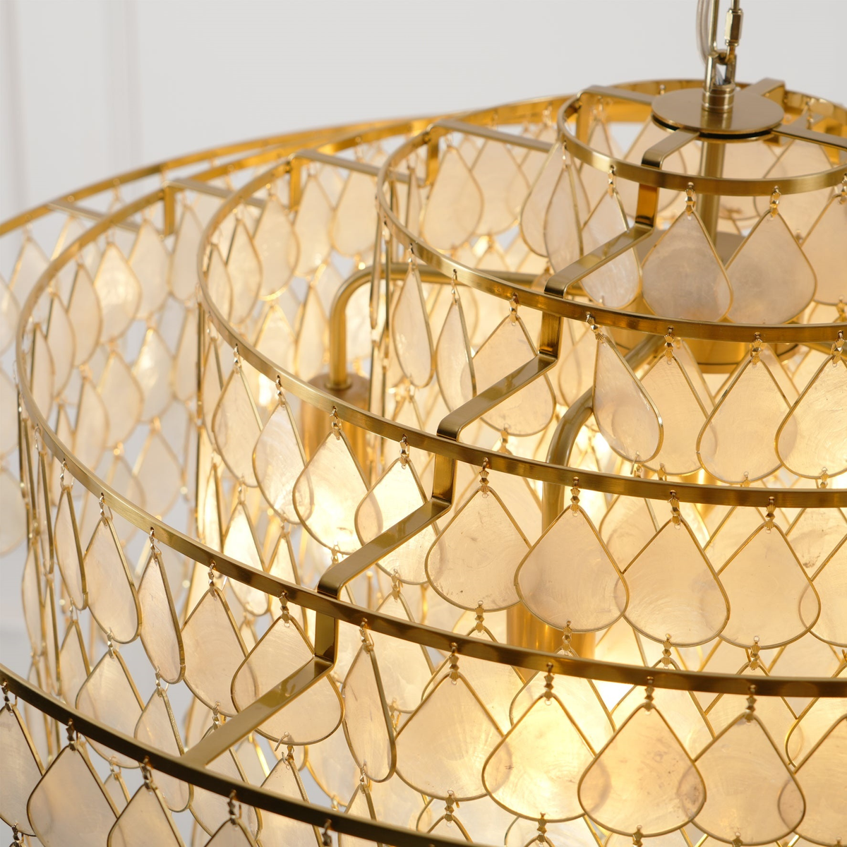 Detail of the gold ring supports and teardrop shell discs on this Clérachic chandelier, seen from below with the bulbs glowing.