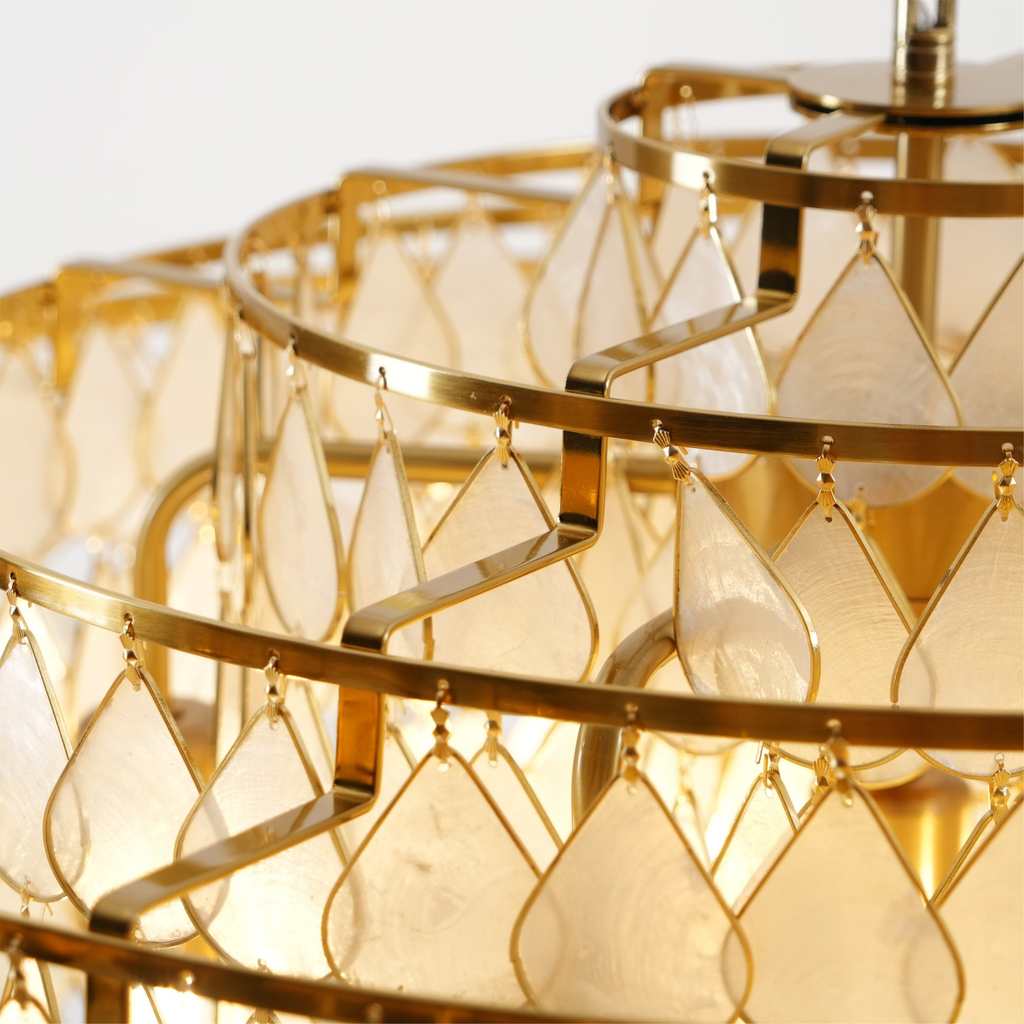 Close view of the gold hooks and the large teardrop capiz shell discs on this Clérachic chandelier, lit warm.
