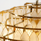 Close view of the gold hooks and the large teardrop capiz shell discs on this Clérachic chandelier, lit warm.