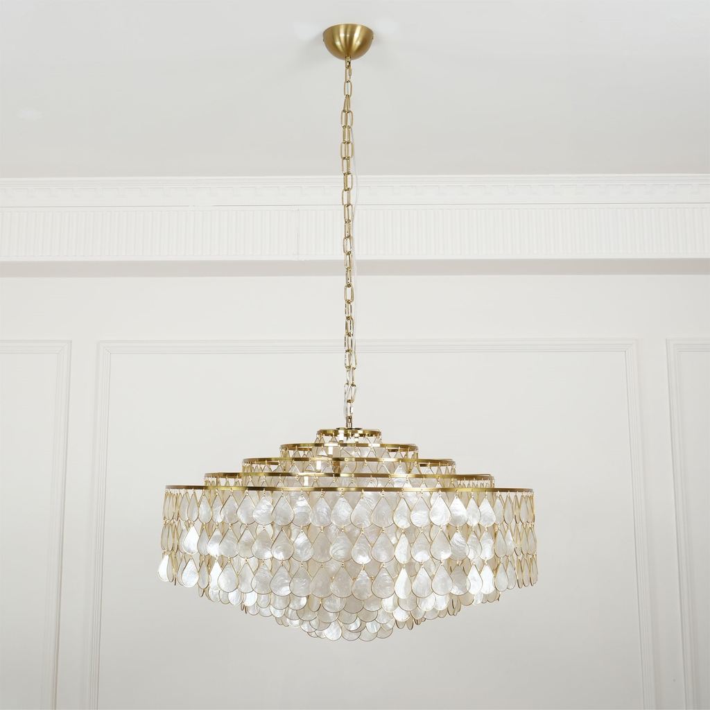 A Clérachic chandelier on a brass canopy and long chain, hung in a white panelled room, its tiers of pearly shell teardrops unlit.