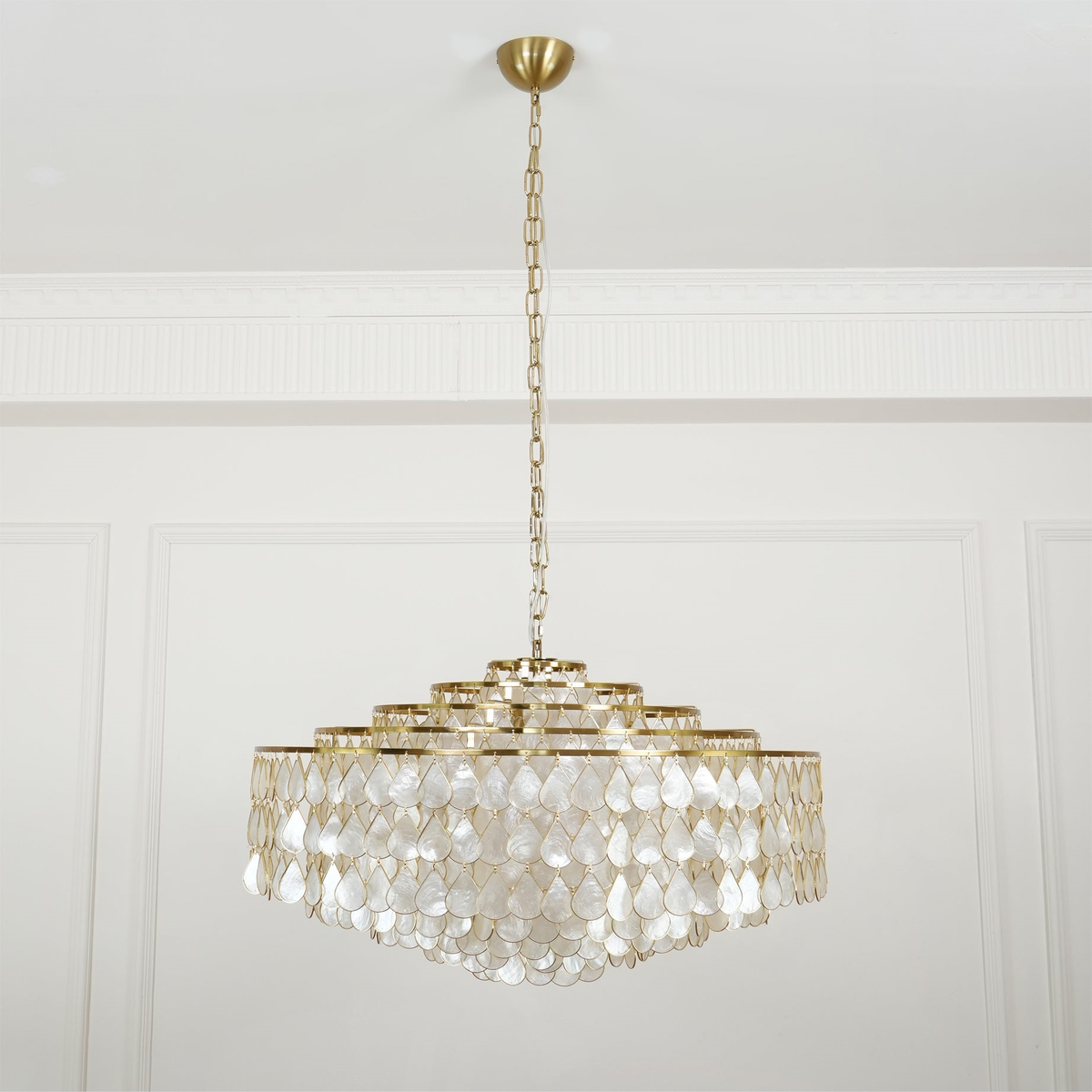A Clérachic chandelier on a brass canopy and long chain, hung in a white panelled room, its tiers of pearly shell teardrops unlit.