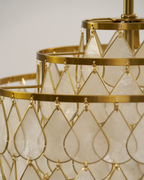 Close view of a teardrop shell disc held in a gold wire loop on this Clérachic chandelier, with gold rings behind it.