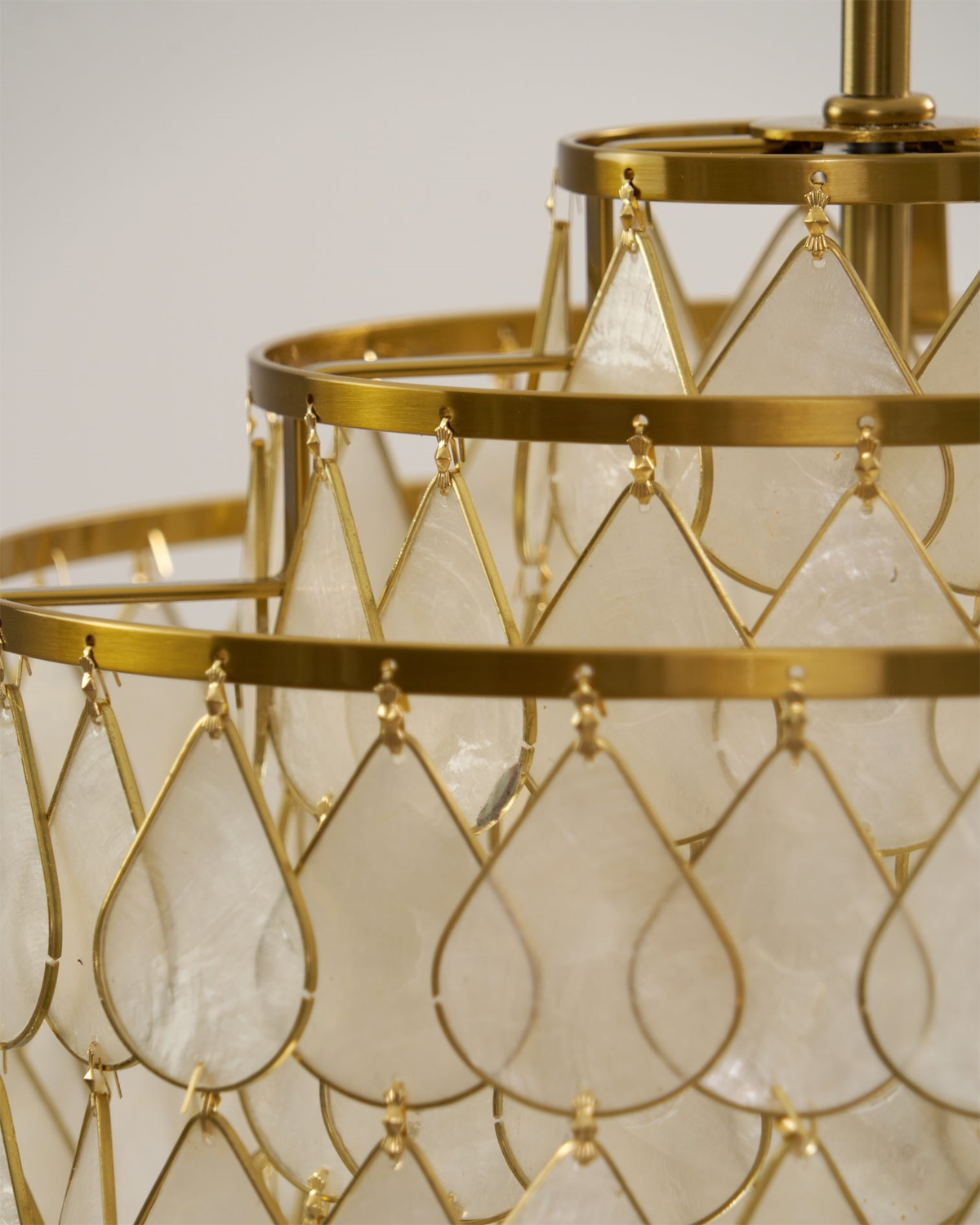 Close view of a teardrop shell disc held in a gold wire loop on this Clérachic chandelier, with gold rings behind it.
