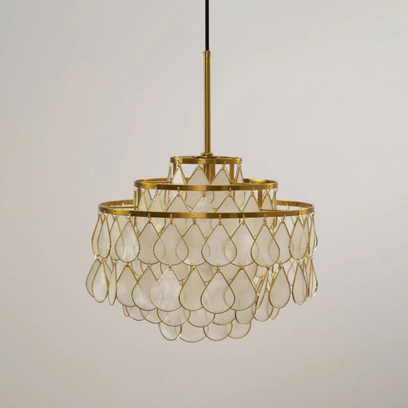 A small Clérachic chandelier on a gold rod and black cord, its three tiers of shell teardrops unlit against a grey backdrop.