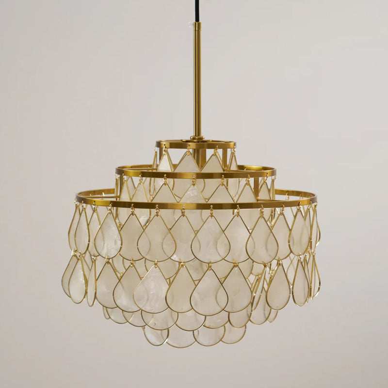 A Clérachic chandelier on a gold rod, shown unlit from a lower angle, with large shell teardrops in gold wire on a pale wall.