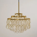 A Clérachic chandelier on a gold rod, shown unlit from a lower angle, with large shell teardrops in gold wire on a pale wall.