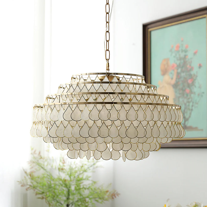 This Clérachic chandelier on a chain hangs beside a framed painting, its stacked gold rings holding rows of unlit shell teardrops.