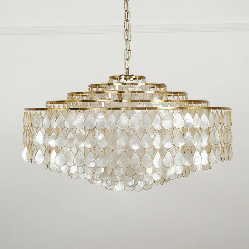 A wide Clérachic chandelier on a chain and gold canopy, with five tiers of pearly shell teardrops on a pale grey wall.
