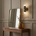 An antique brass Clérachic wall light on a panelled beige wall, above a walnut console with a mirror and an amber vase.