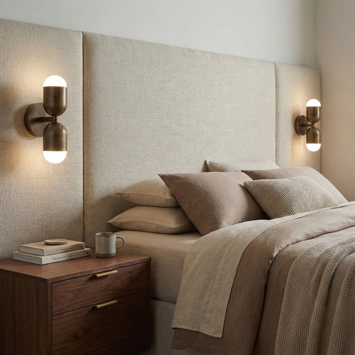 Two antique brass Clérachic wall lights on either side of a linen headboard, above walnut bedside tables.