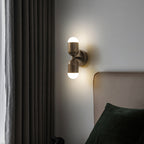 An antique brass Clérachic wall light beside a charcoal curtain, glowing softly above a bed with a dark green cushion.