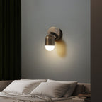 Antique brass Clérachic wall light on a grey wall, tilted toward a made bed with white pillows.