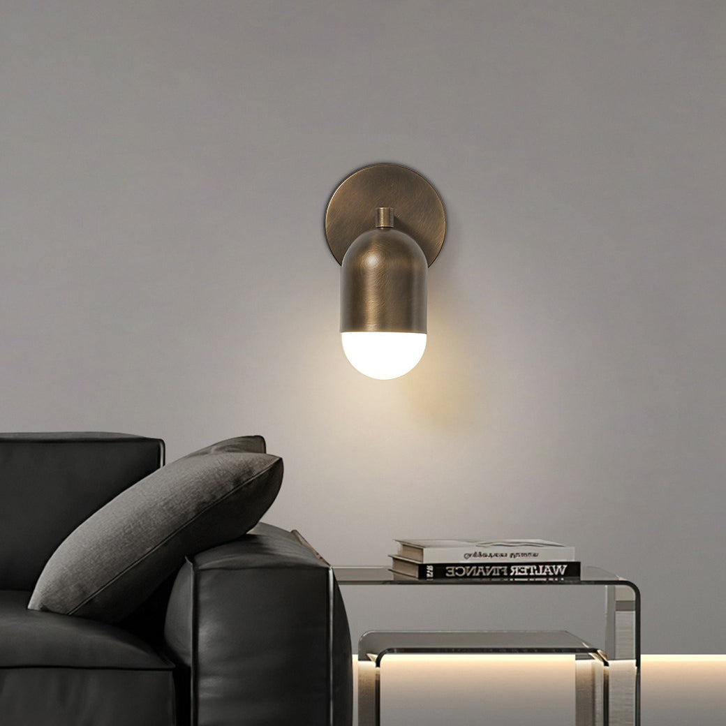 An antique brass Clérachic wall light with a downward capsule shade, above a black leather sofa and a glass side table.