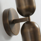 Close view of the brushed antique brass backplate and joint between the two capsules of this Clérachic wall light.