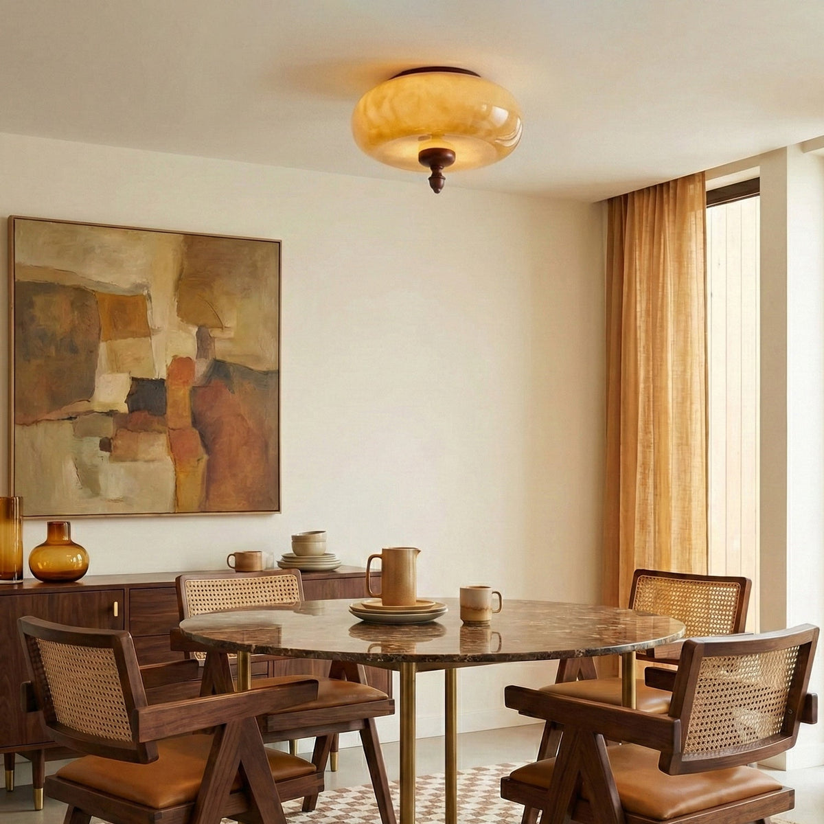 A Clérachic caramel glass ceiling light above a round marble-topped dining table with rattan chairs, beside a gold curtain.