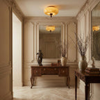 Two reflections of this Clérachic caramel glass ceiling light, one hanging in a panelled hallway and one in the mirror over a carved wooden console.