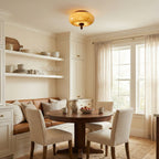 Small Clérachic caramel glass ceiling light over a round wooden table in a breakfast nook with a built-in bench and open shelves.