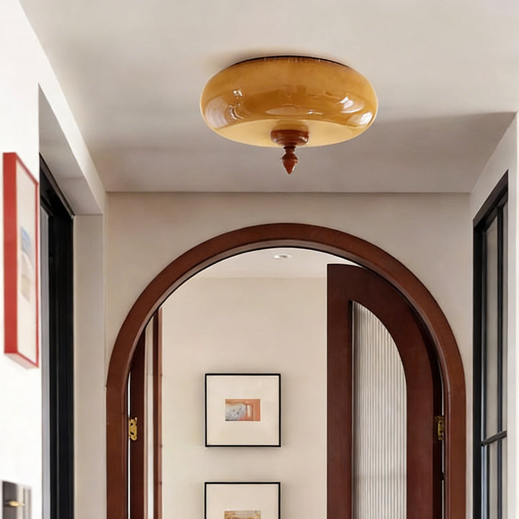 Looking up at a Clérachic caramel glass flush-mount light in a hallway with a dark wooden arched doorway beyond.