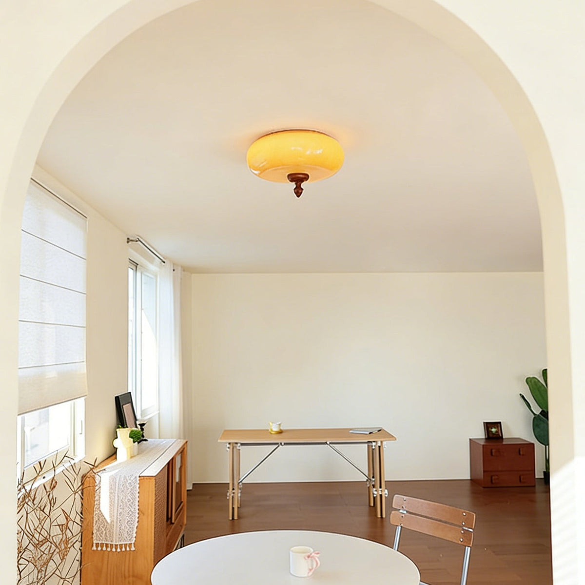 Warm amber Clérachic ceiling light glowing in an arched, cream-walled room with a wooden desk and a white round table.