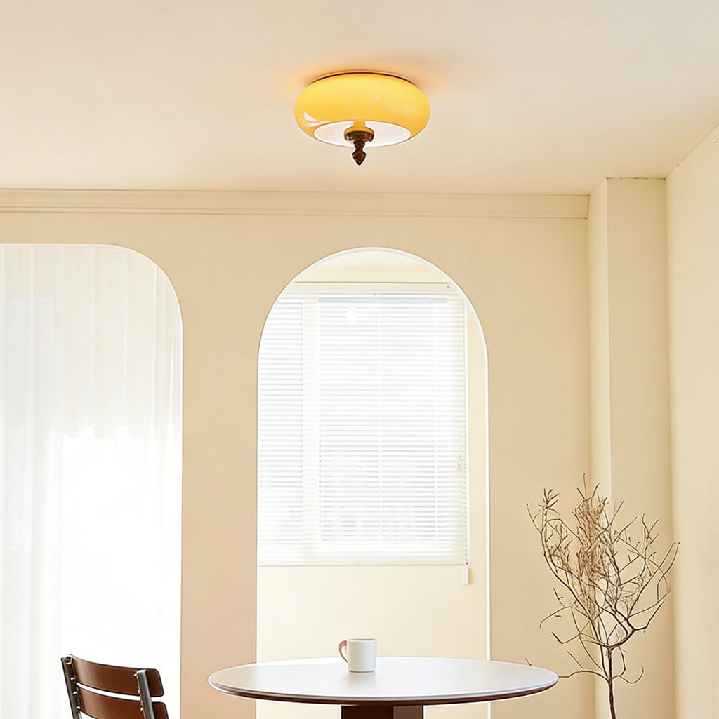 A lit Clérachic caramel glass ceiling light seen from below in a cream room with two arched windows and a small round table.