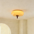 Close-up from below of the glowing amber glass shade and walnut finial of this Clérachic ceiling light against a cream ceiling.