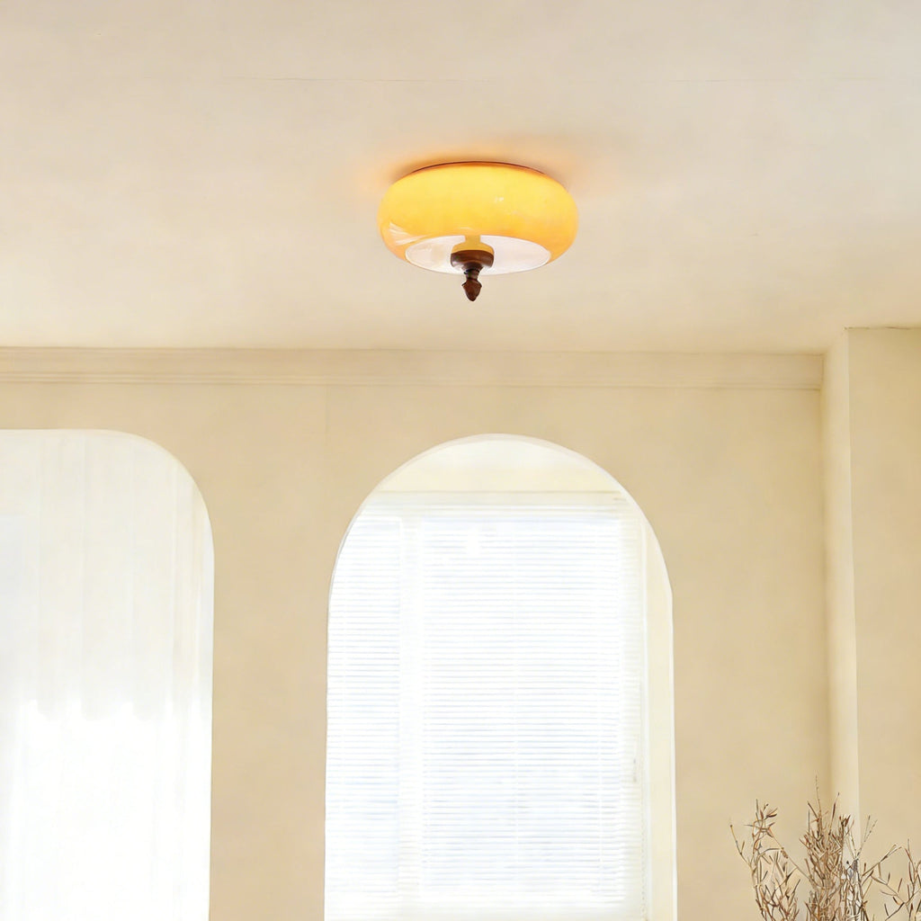 Clérachic caramel glass ceiling light switched on above a cream room with arched windows and sheer white curtains.