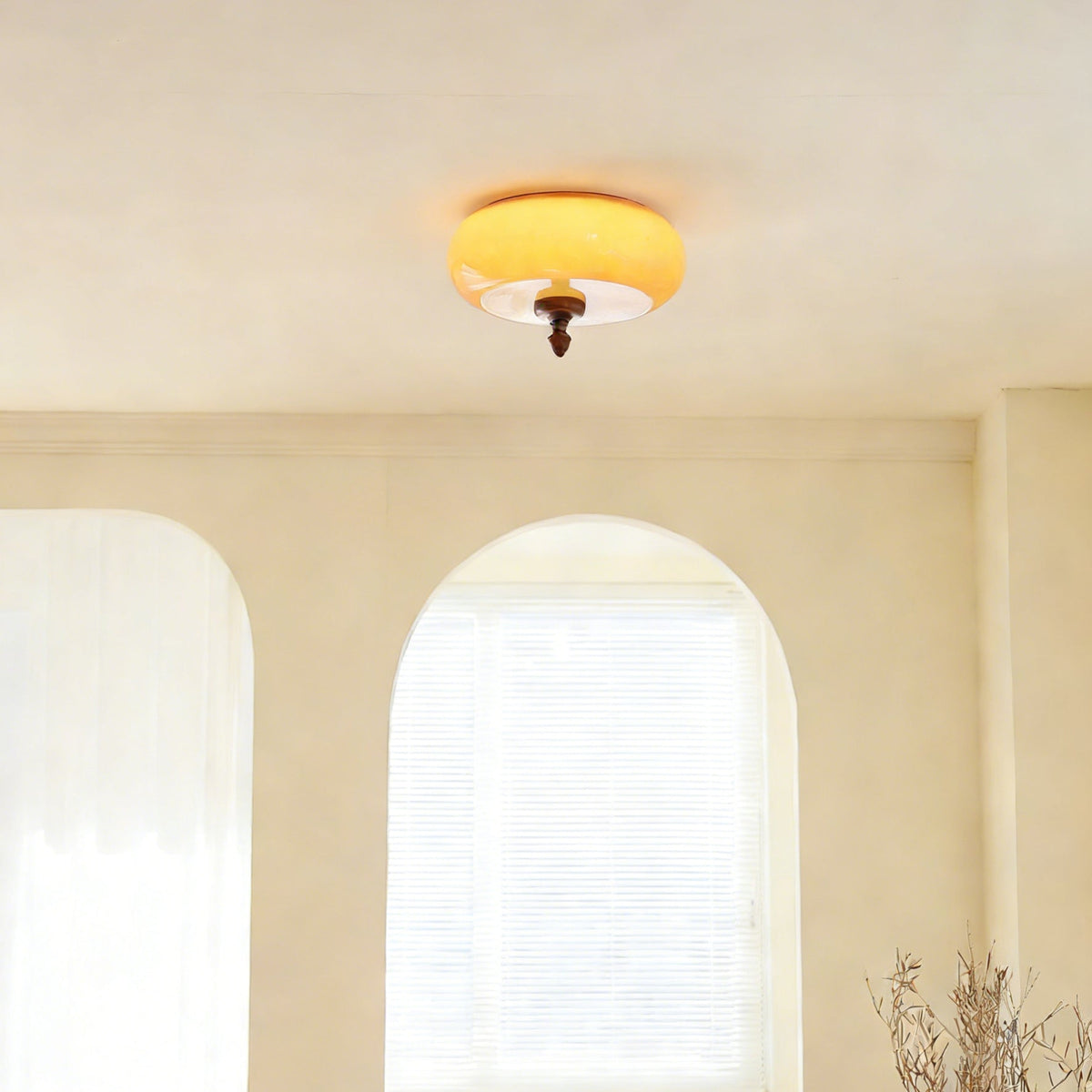 Clérachic caramel glass ceiling light switched on above a cream room with arched windows and sheer white curtains.
