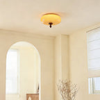 A distant view of this Clérachic caramel glass light on the ceiling of a bright room with an arched window and dried branches.