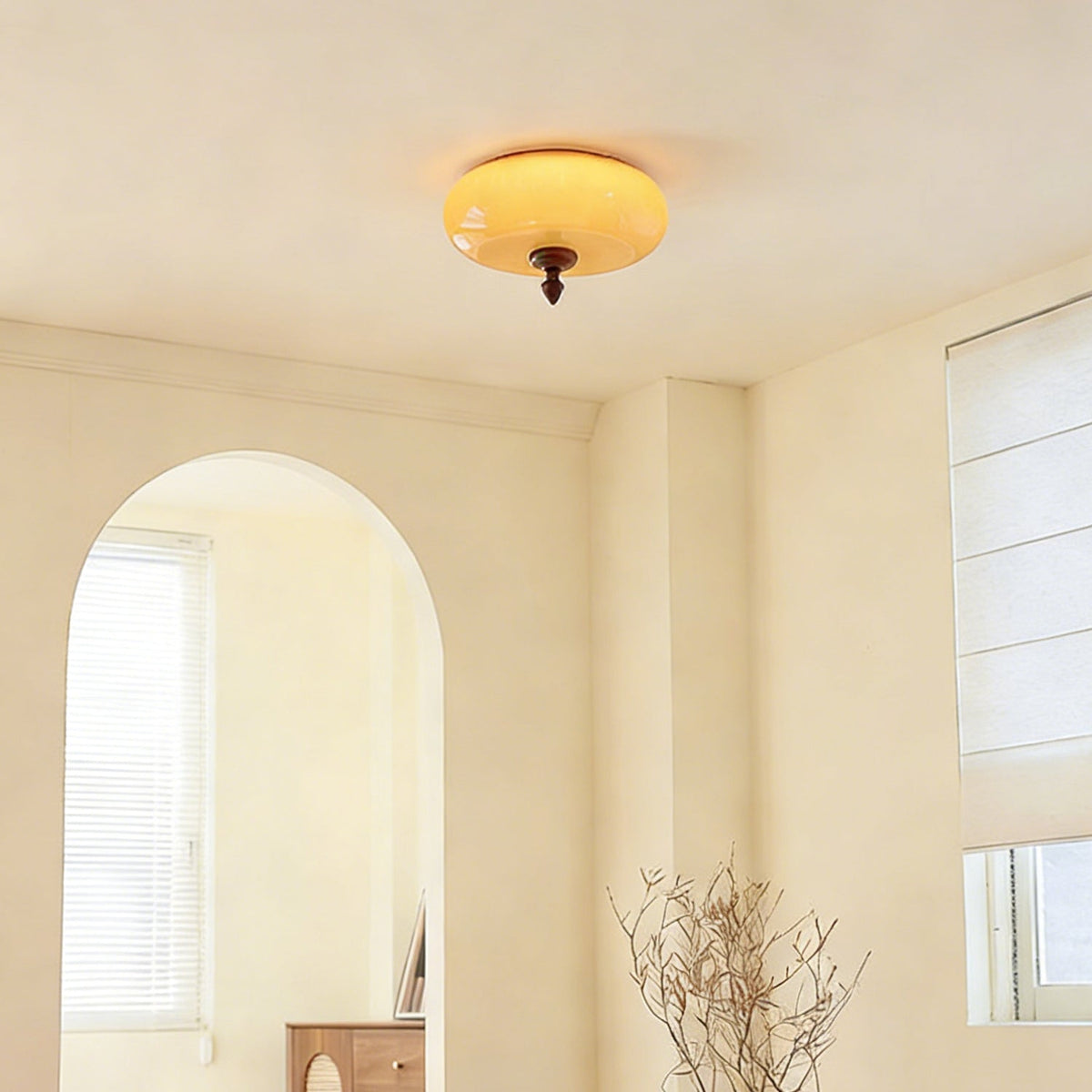 A distant view of this Clérachic caramel glass light on the ceiling of a bright room with an arched window and dried branches.