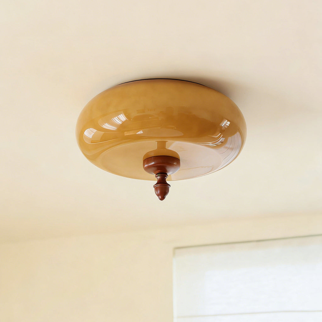 Unlit caramel glass shade with its walnut-toned finial, this Clérachic flush-mount light seen from below against a pale ceiling.