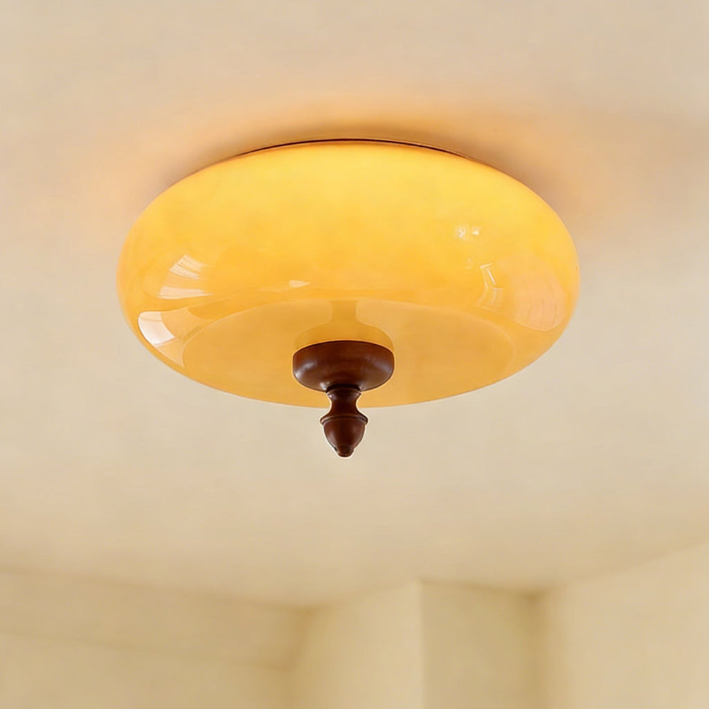 The caramel glass shade of this Clérachic ceiling light lit up, glowing yellow-amber above its walnut-toned turned finial.