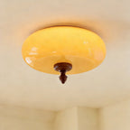 The caramel glass shade of this Clérachic ceiling light lit up, glowing yellow-amber above its walnut-toned turned finial.