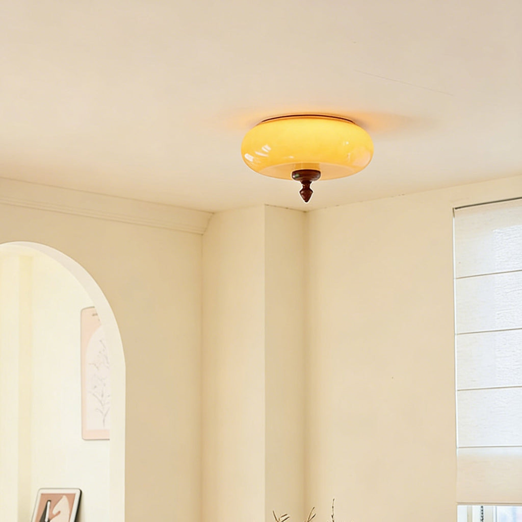 Lit Clérachic ceiling light with a caramel glass shade, shown in the corner of a cream room beside an arched opening and a window blind.
