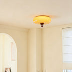 Lit Clérachic ceiling light with a caramel glass shade, shown in the corner of a cream room beside an arched opening and a window blind.