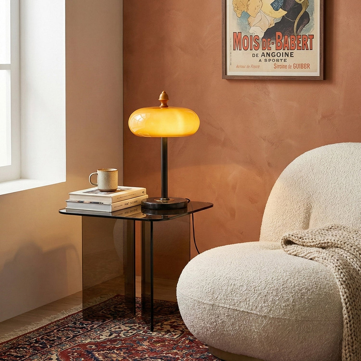 A lit Clérachic caramel glass lamp on a smoked-glass side table beside a cream bouclé chair and a terracotta wall.