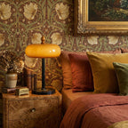 Clérachic caramel dome lamp on a burr-wood bedside table, set against floral wallpaper and rust and mustard bed linen.
