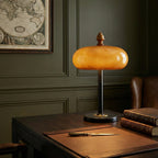 The Clérachic dome lamp on a dark desk beside leather-bound books, with green panelled walls and a framed map behind.