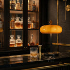 Glowing caramel glass lamp from Clérachic on a black marble bar top, with whisky decanters and a tumbler in the cabinet behind.