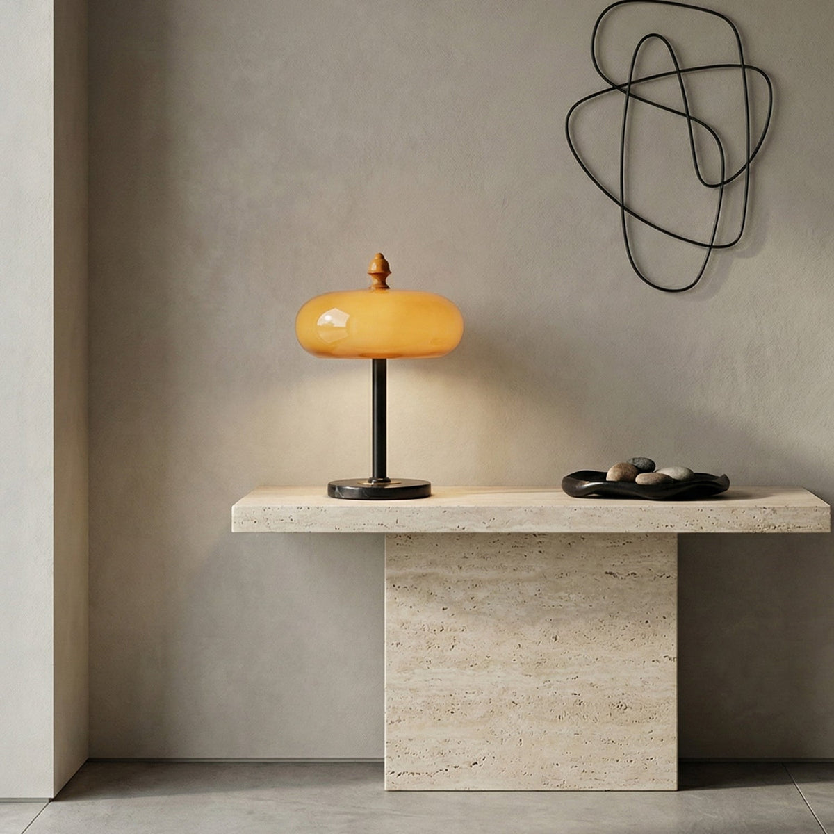A Clérachic table lamp on a travertine console against a grey plaster wall, with a looping black wire sculpture above.