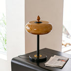 Unlit view of the Clérachic lamp, its glossy brown-amber dome glass and wooden finial above a black base with a brass ring.