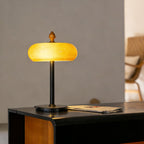 Clérachic lamp switched on, the glass dome glowing pale yellow above a thin black stem on a dark console with a wooden end.